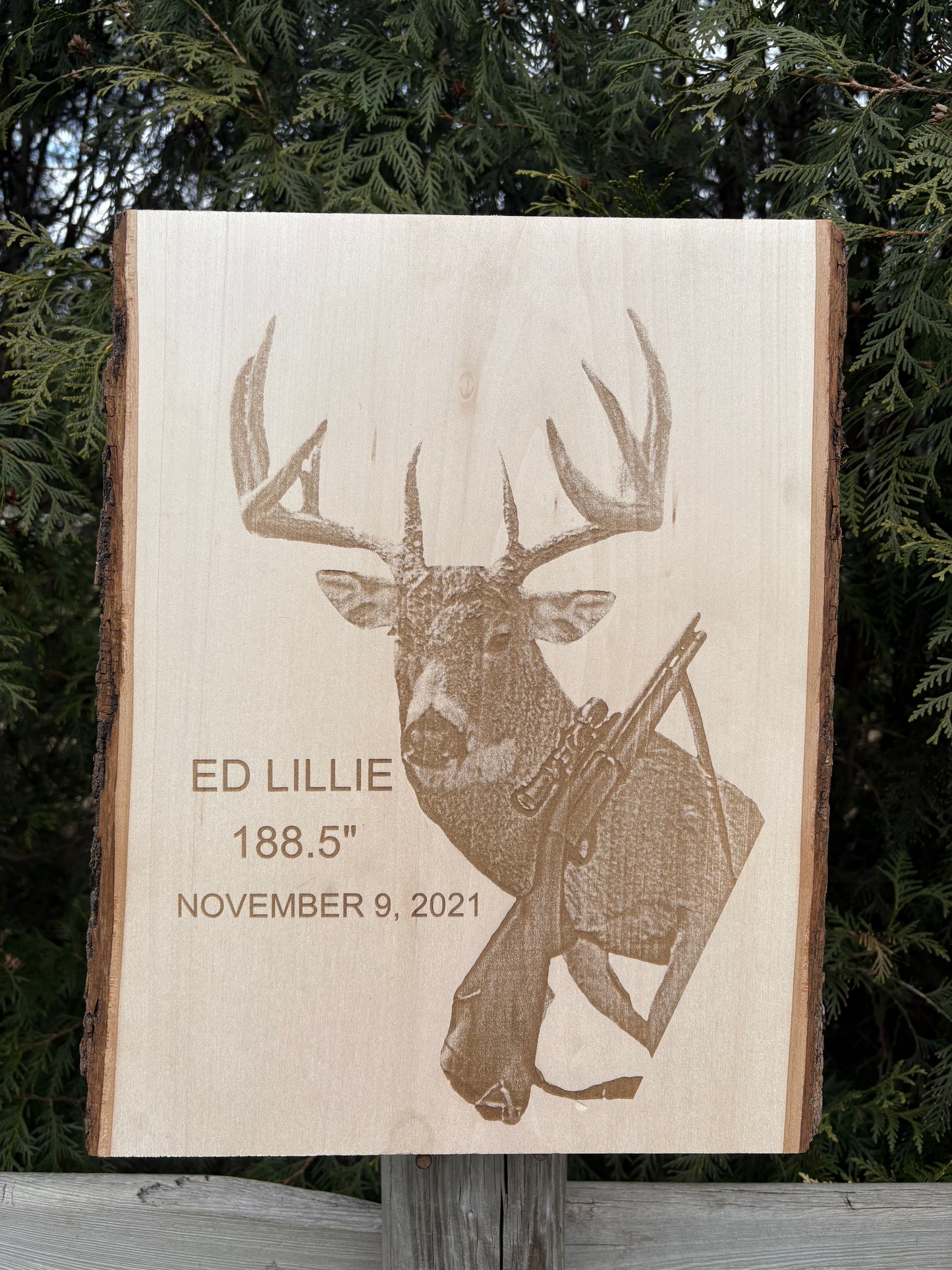 Wooden plaque with engraved deer and hunting gear, set against a natural background.